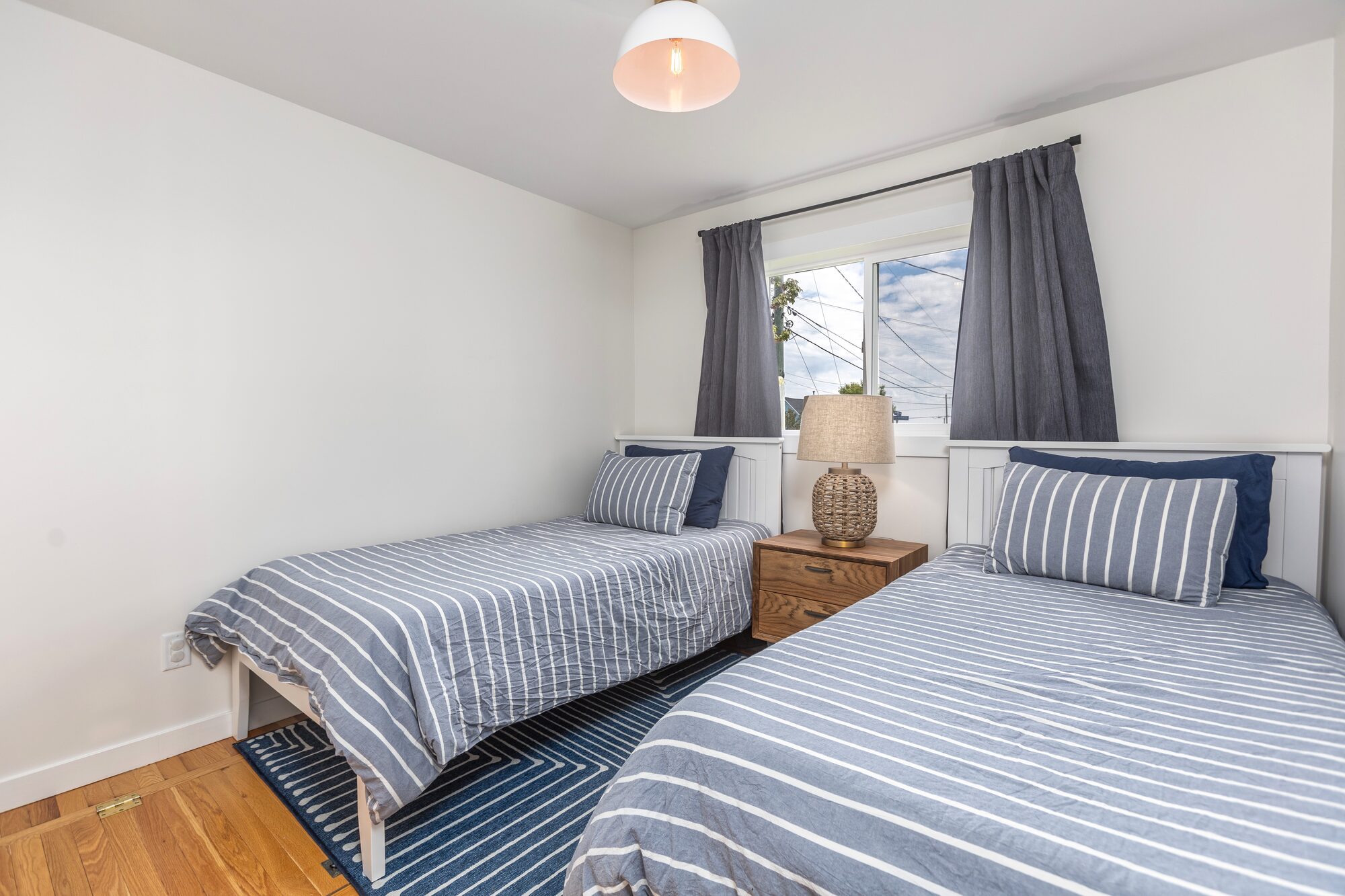 The twin room with two beds dressed in blue-striped linen, navy curtains, and a soft striped rug.